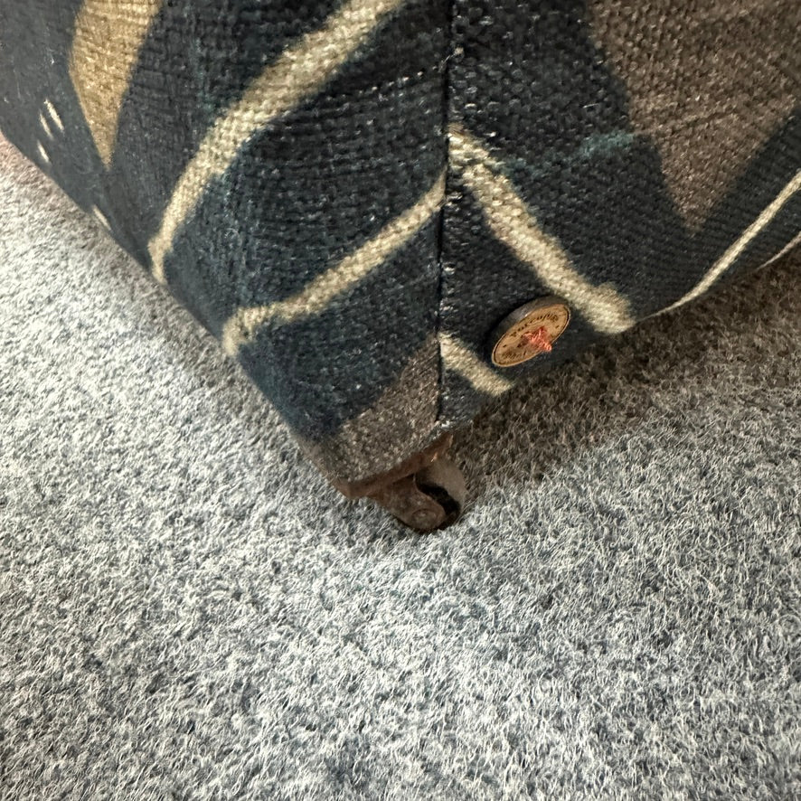 Close-up of a woven upholstered furniture corner with a dark gray, beige, and black plaid pattern, resting on a gray textured carpet.