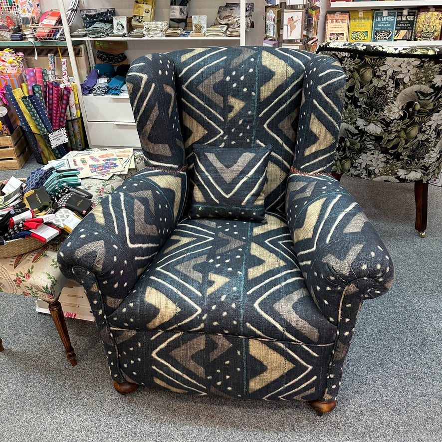 An armchair upholstered in a dark navy blue fabric with beige and white geometric patterns, shown in a retail store setting.