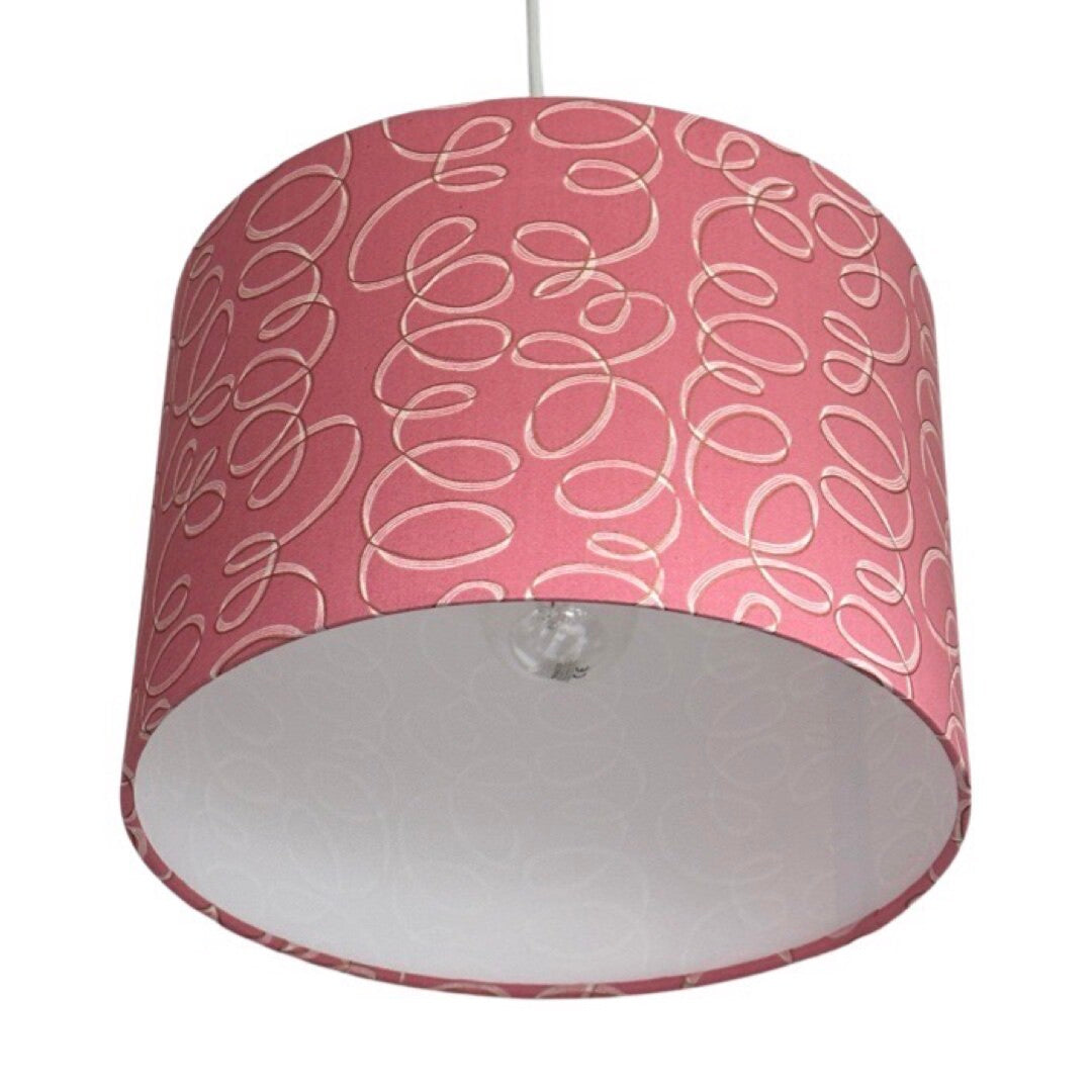 Close up of a drum lampshade covered in pink cotton fabric with white and gold ribbons