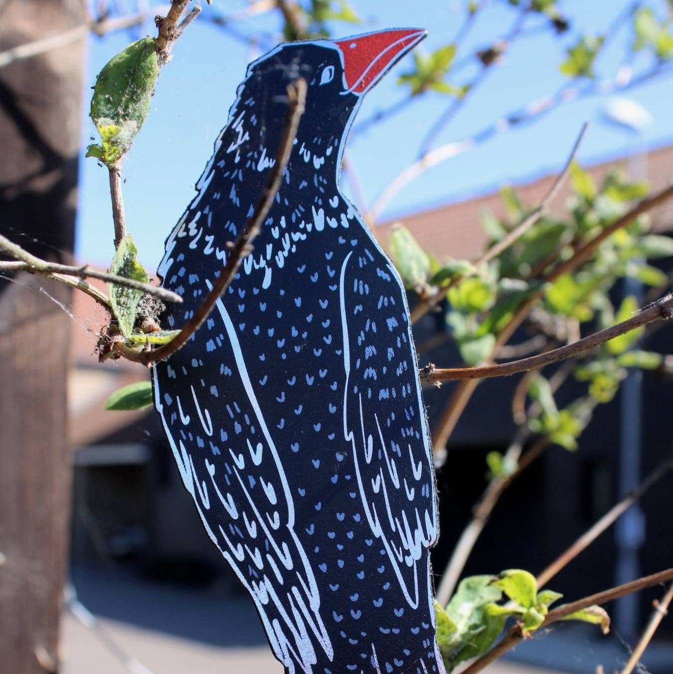 Decorative bird bookmark with black, white, and red colors on a branch.