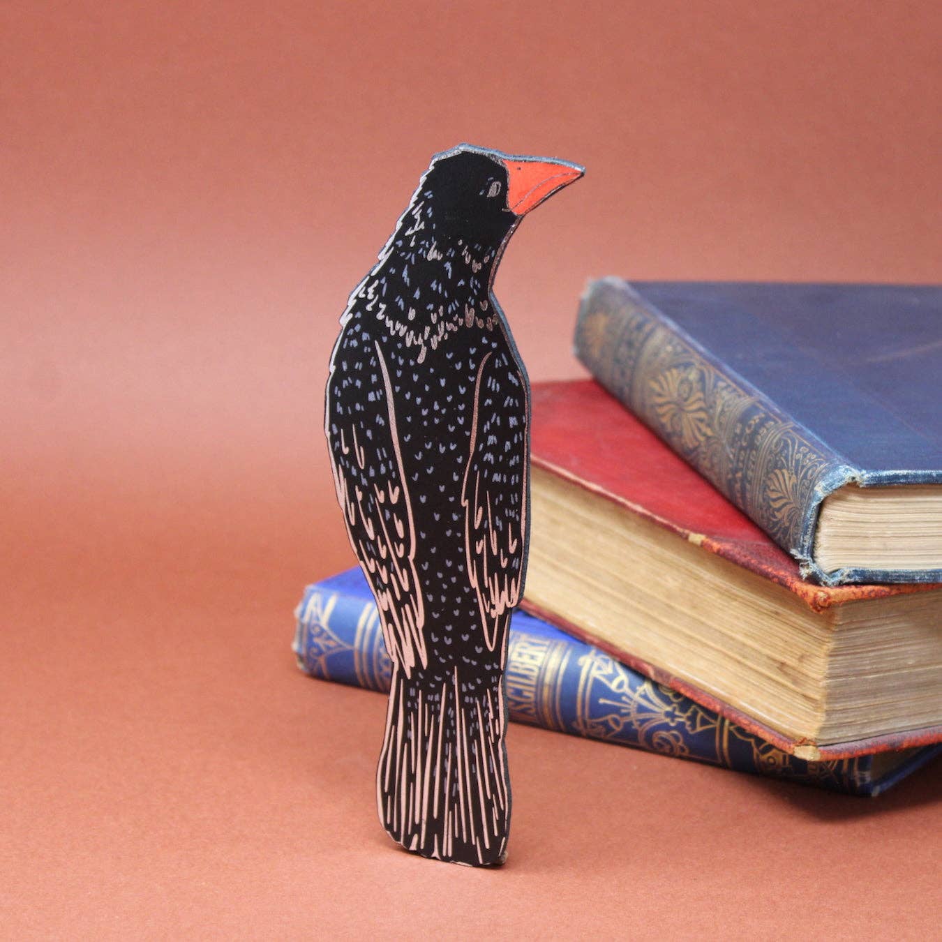 Bird bookmark on a stack of books with a pinkish-brown background.