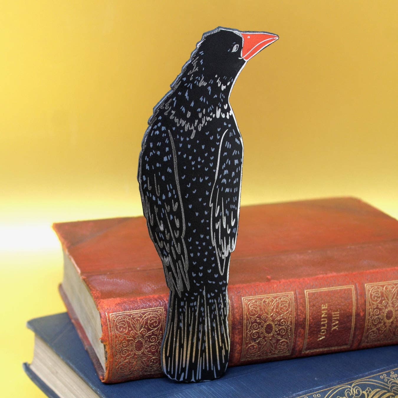Black bird-shaped object on top of a stack of books with a yellow background.