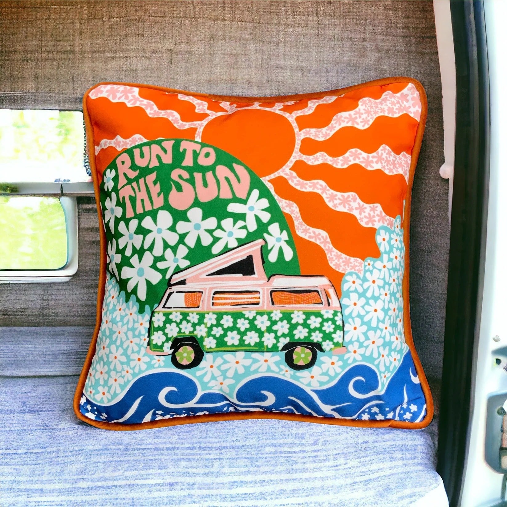 Decorative pillow with a van and sun design on a vehicle seat.
