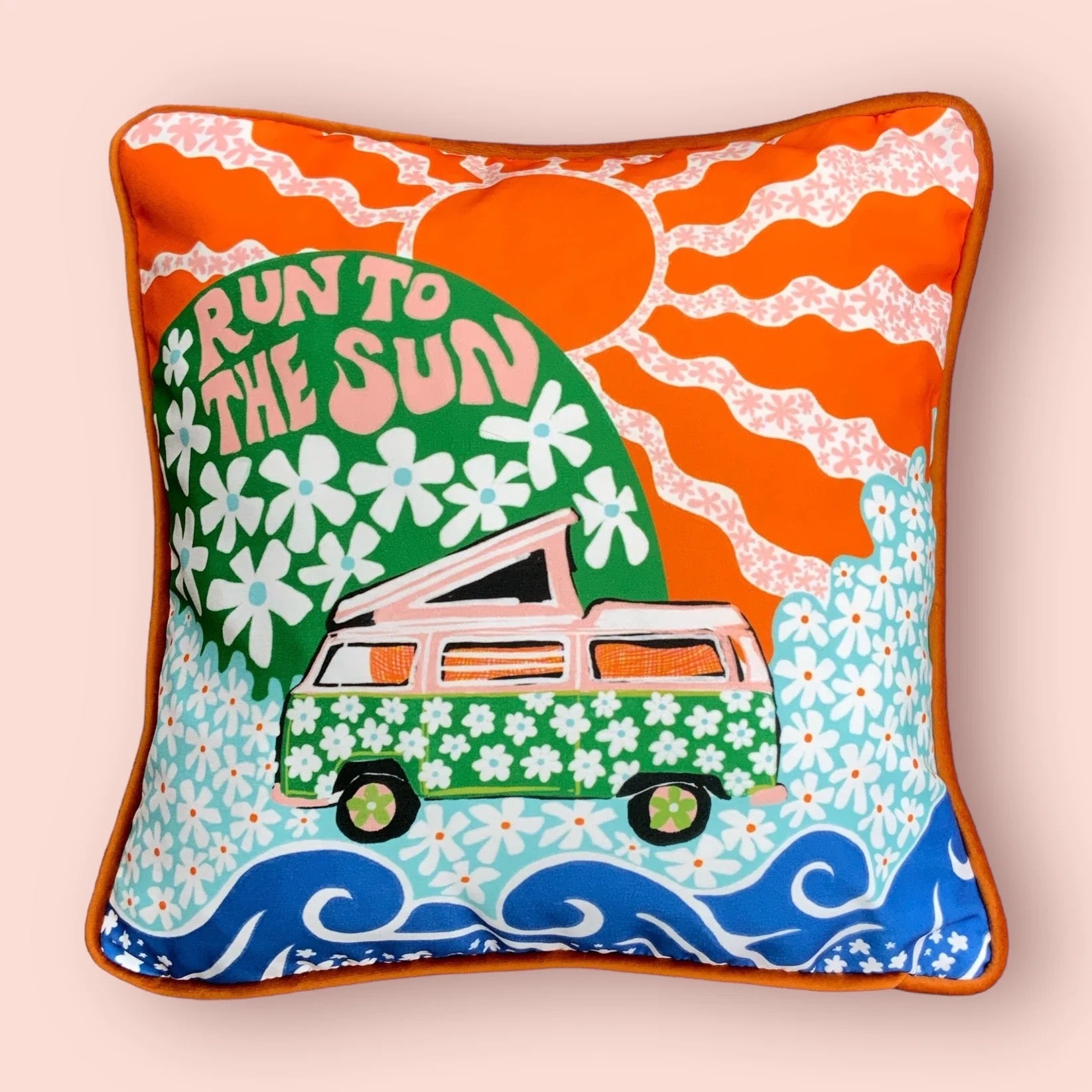 Decorative pillow with a van, sun, and floral design on a light pink background.