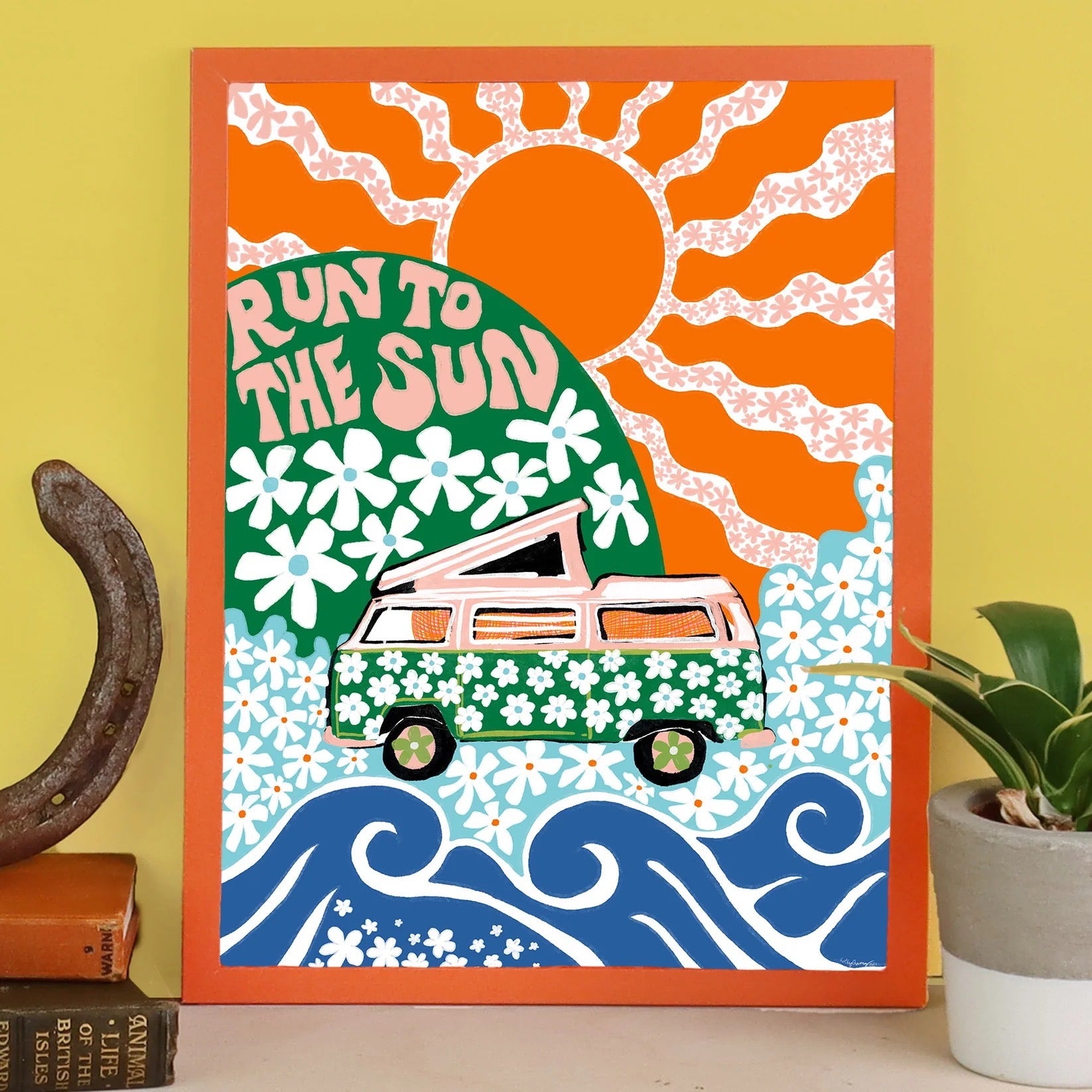 Framed artwork with a van, sun, and floral design on a yellow wall.