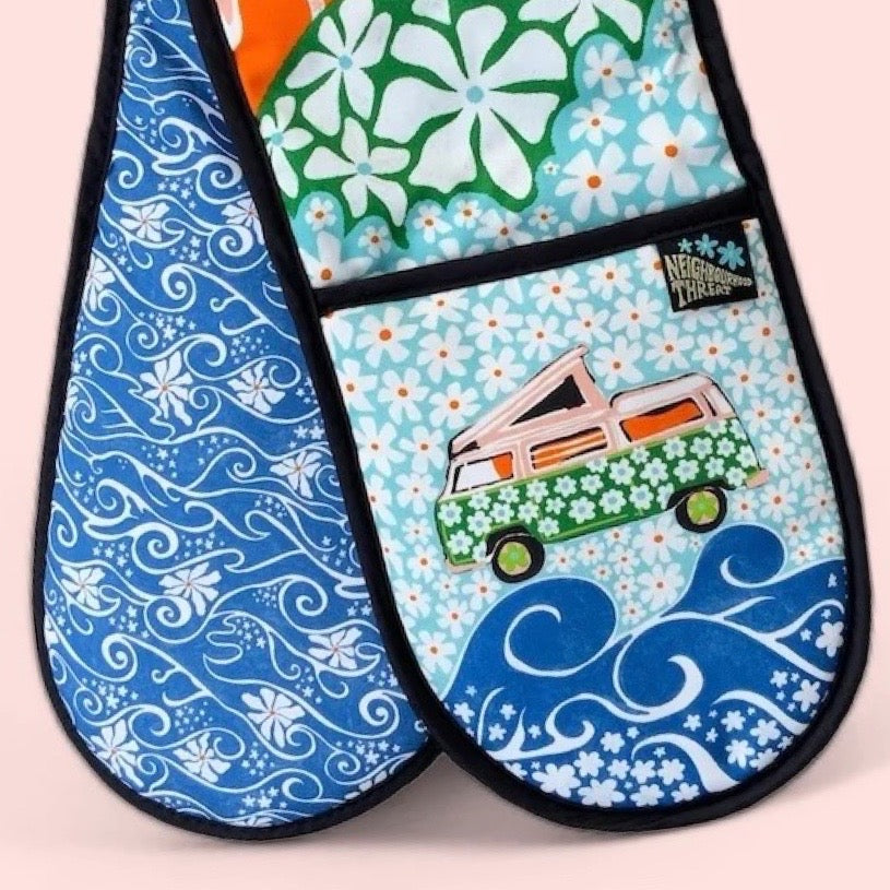 Colourful oven gloves with a pink campervan covered in green daisies against a background of blue daisies.