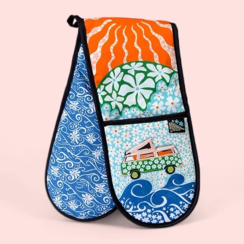 Colourful oven gloves with a pink campervan covered in green daisies against a background of blue daisies.