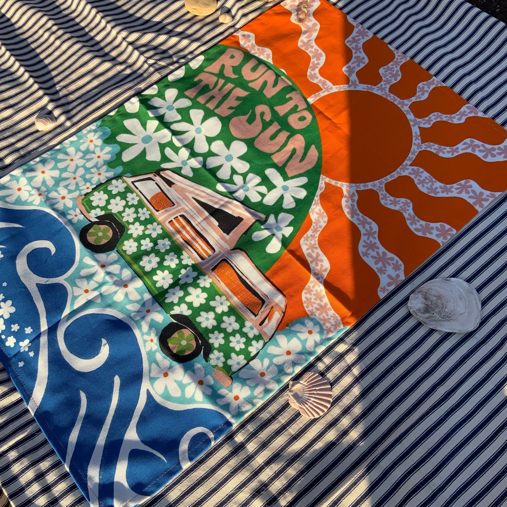 Colourful fabric with a sun, car, and floral patterns on a striped background.