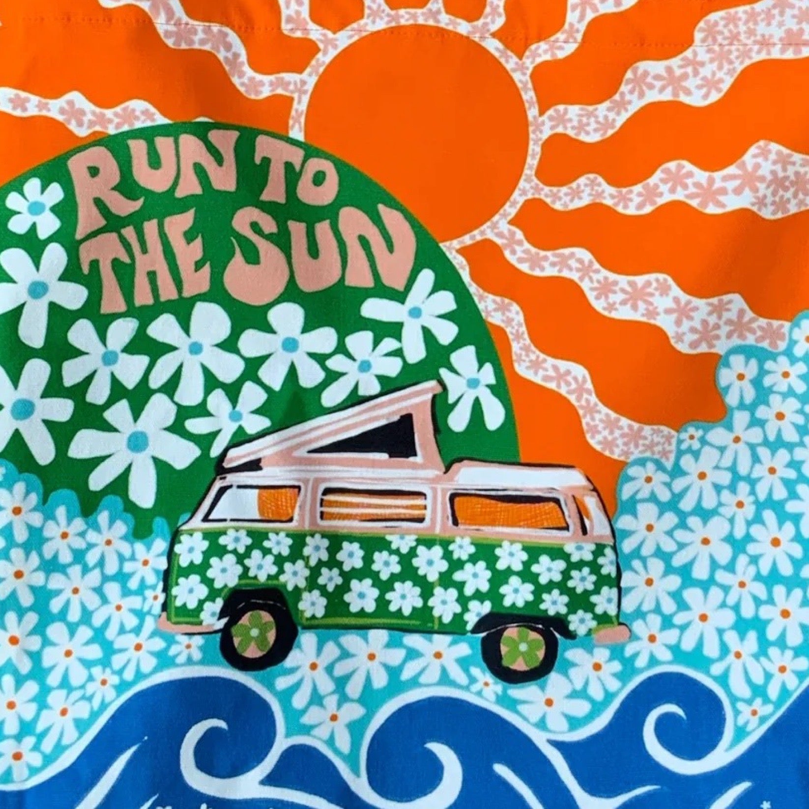 A fabulous, bright and colourful tote bag featuring a pink campervan covered in green daisies on a meadow of blue daisies, a large orange sun and blue waves.