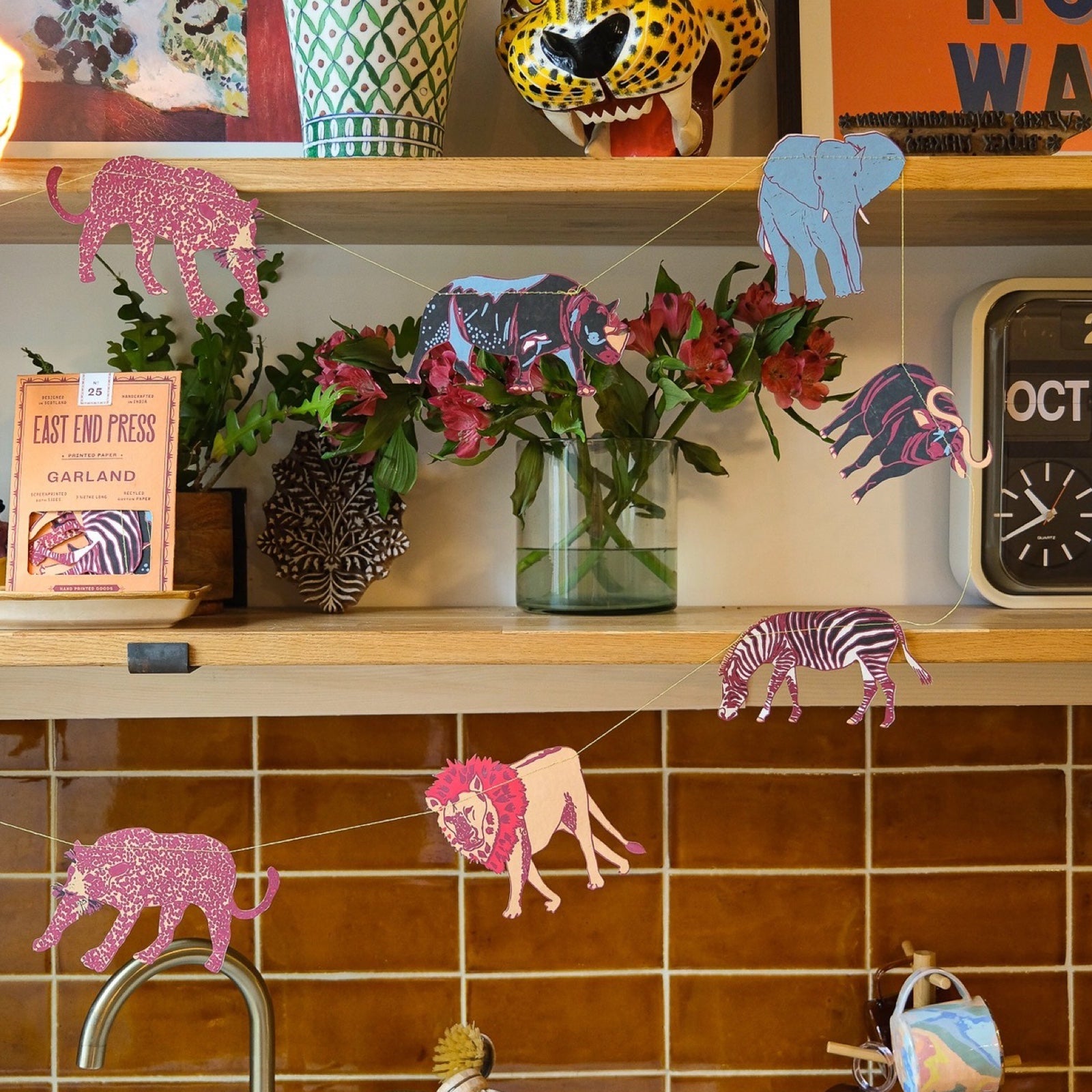 A safari paper garland with ten screen-printed paper animals including zebras, rhinos, elephants and lions in blue, black, white and orange hanging in a kitchen.