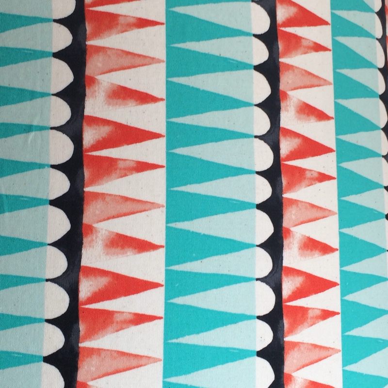 Fabric with rows of turquoise, burnt orange and black shapes against a cream background.