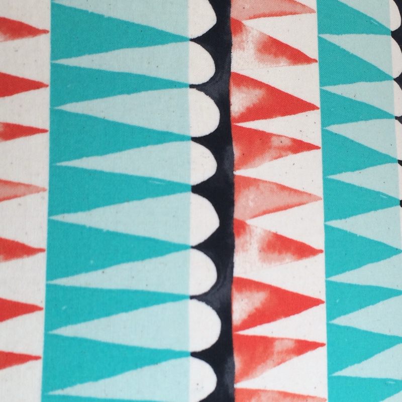 Fabric with rows of turquoise, burnt orange and black shapes against a cream background.