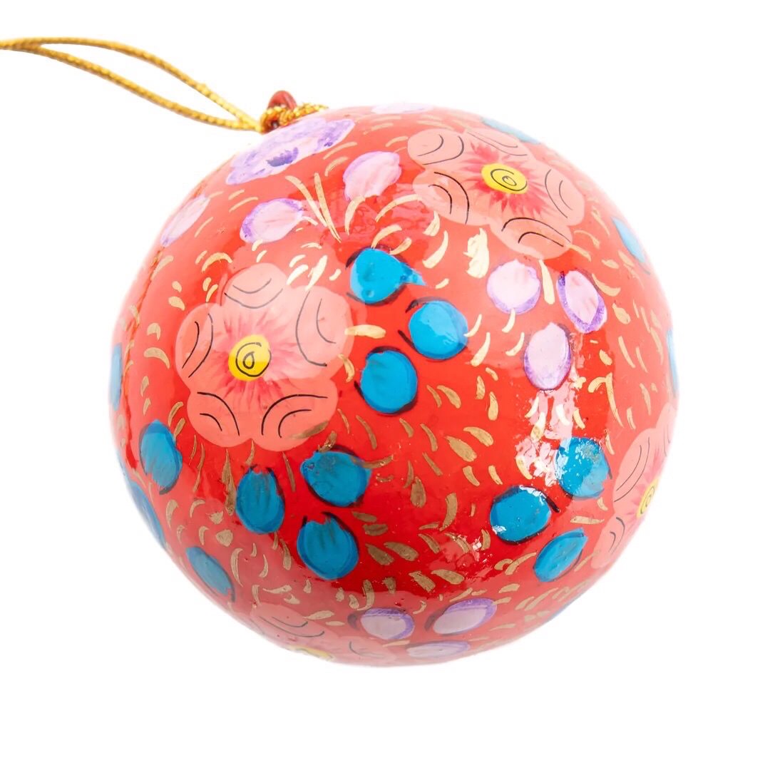 A round papier mache bauble in red with a lilac, blue and red floral design.