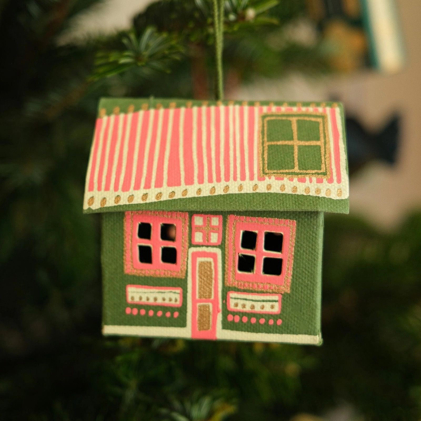 A green and pink Scottish bothy three-dimensional cardboard decoration hanging on a Christmas tree.