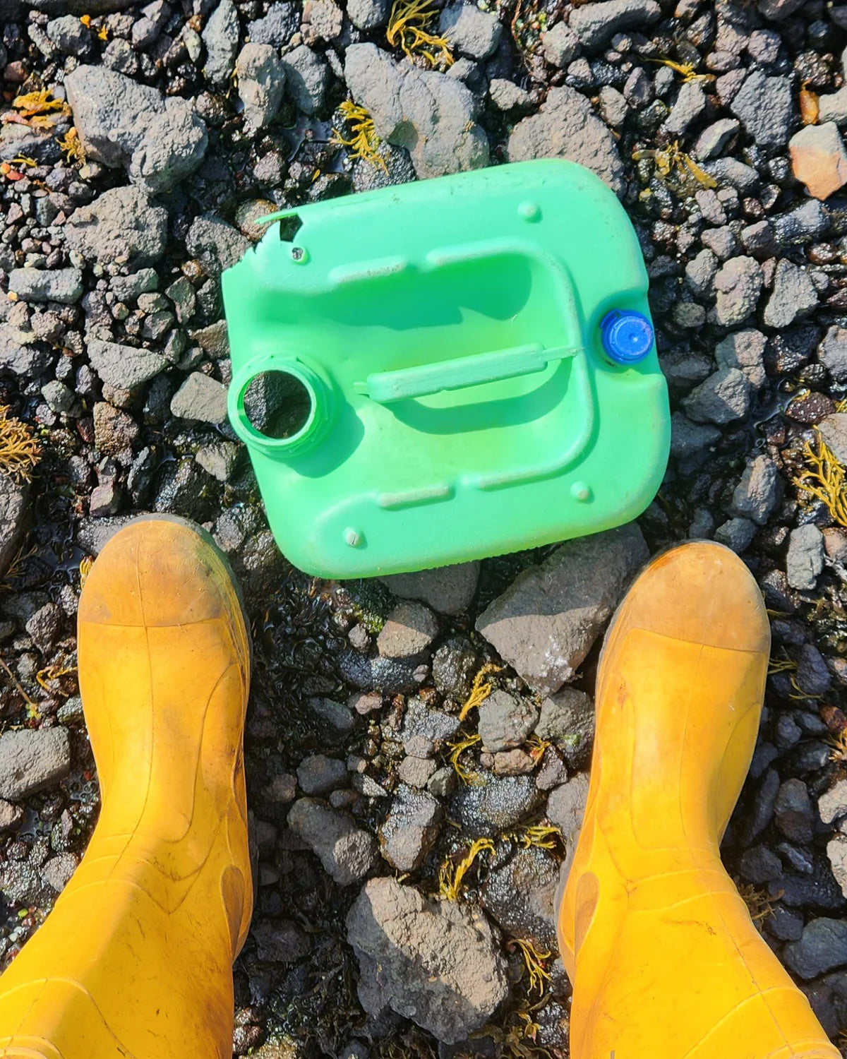 Green plastic container on a rocky ground with yellow boots.
