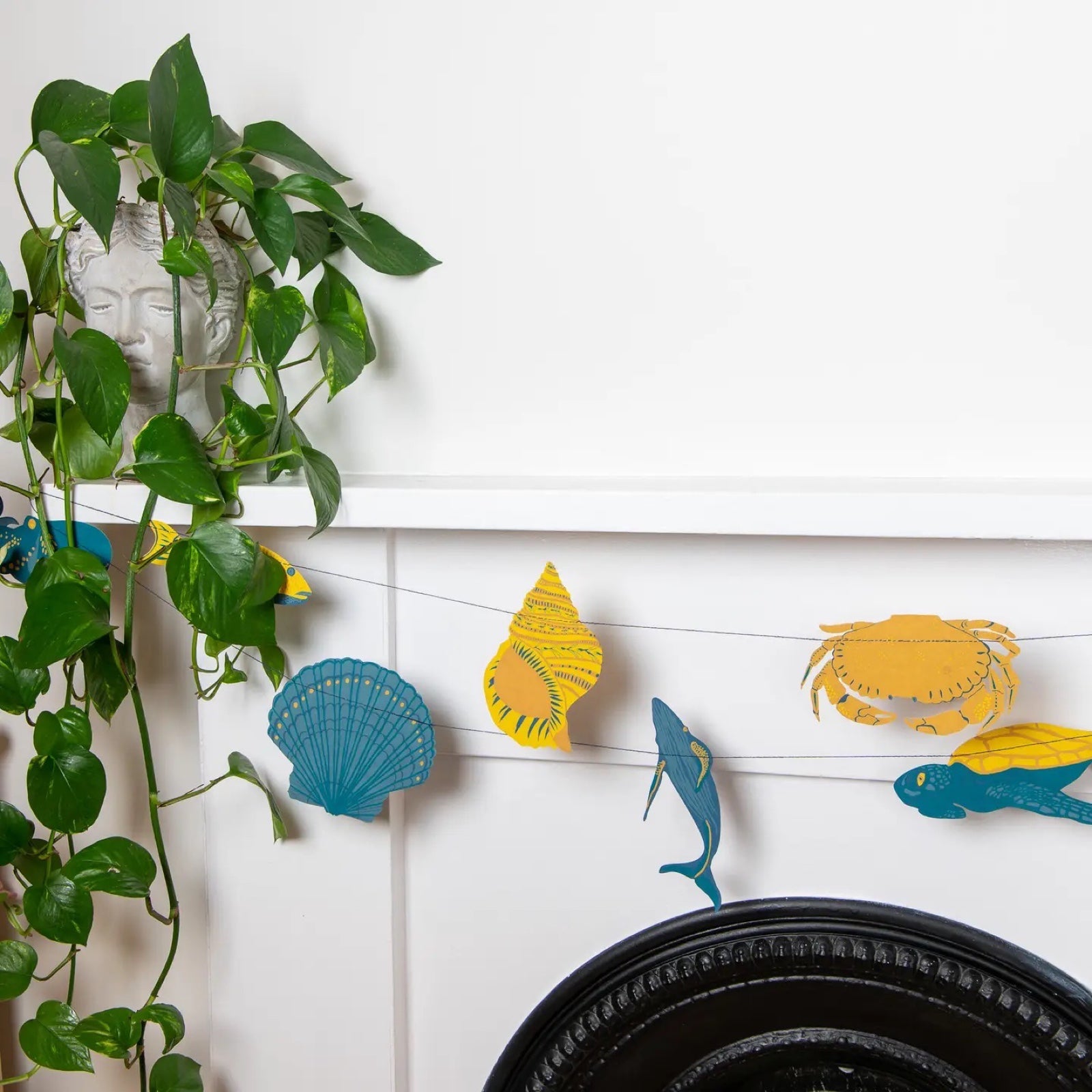 A sealife paper garland featuring ten screen-printed paper seashells, fish, crabs and turtles in blue and yellow hanging against a white wall.