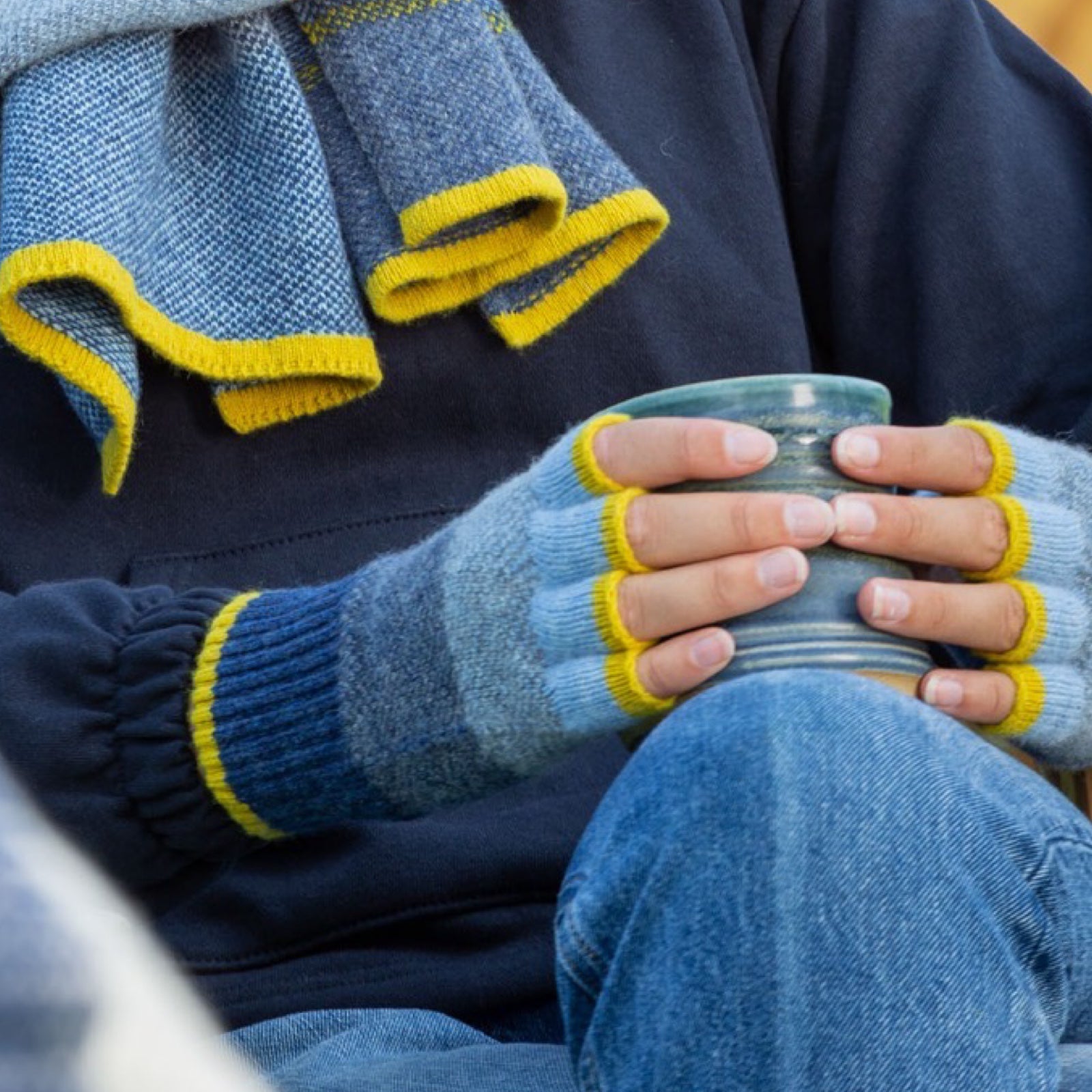 Person wearing blue and yellow gloves holding a cup.