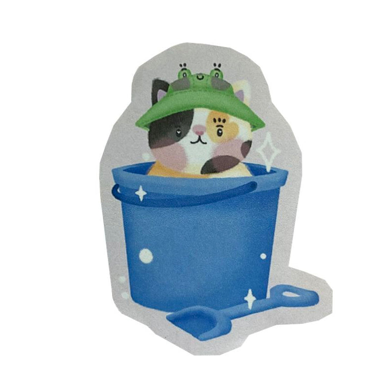 Handmade sticker of a calico cat wearing a frog bucket hat, inside a blue seaside bucket with a matching spade.