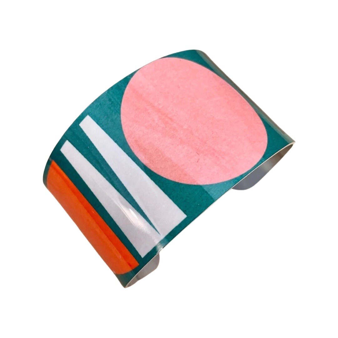 Wide cuff bracelet featuring a multicoloured shapes design on a green background.