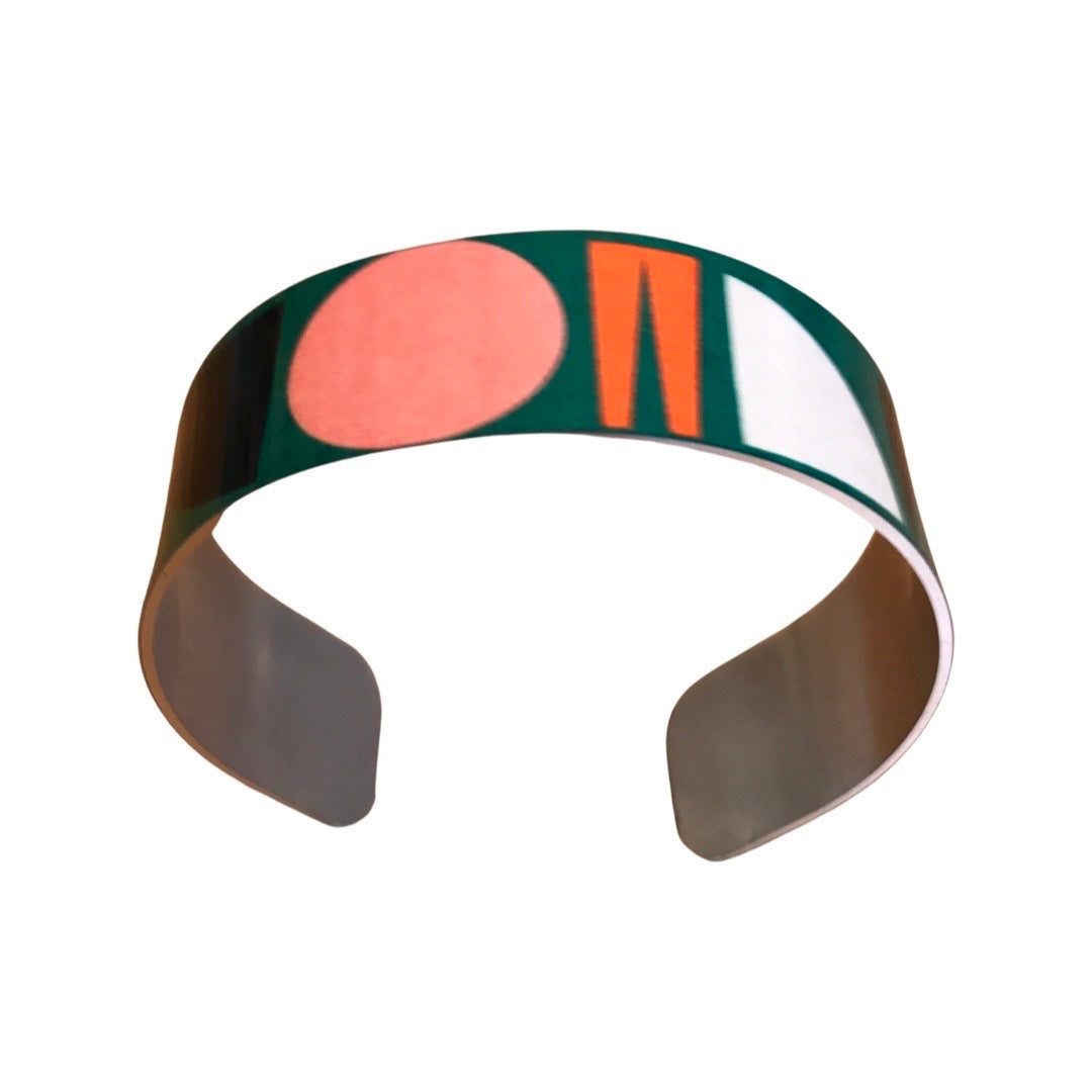 Narrow cuff bracelet featuring a multicoloured shapes design on a green background.