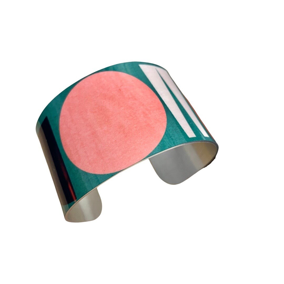 Wide cuff bracelet featuring a multicoloured shapes design on a green background.
