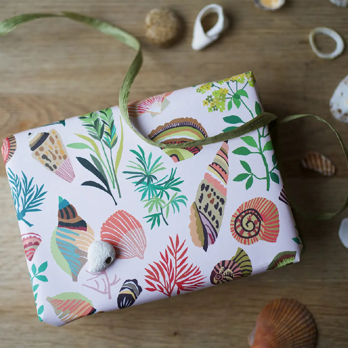 Present wrapped in shell wrapping paper, surrounded by shells and a ribbon.
