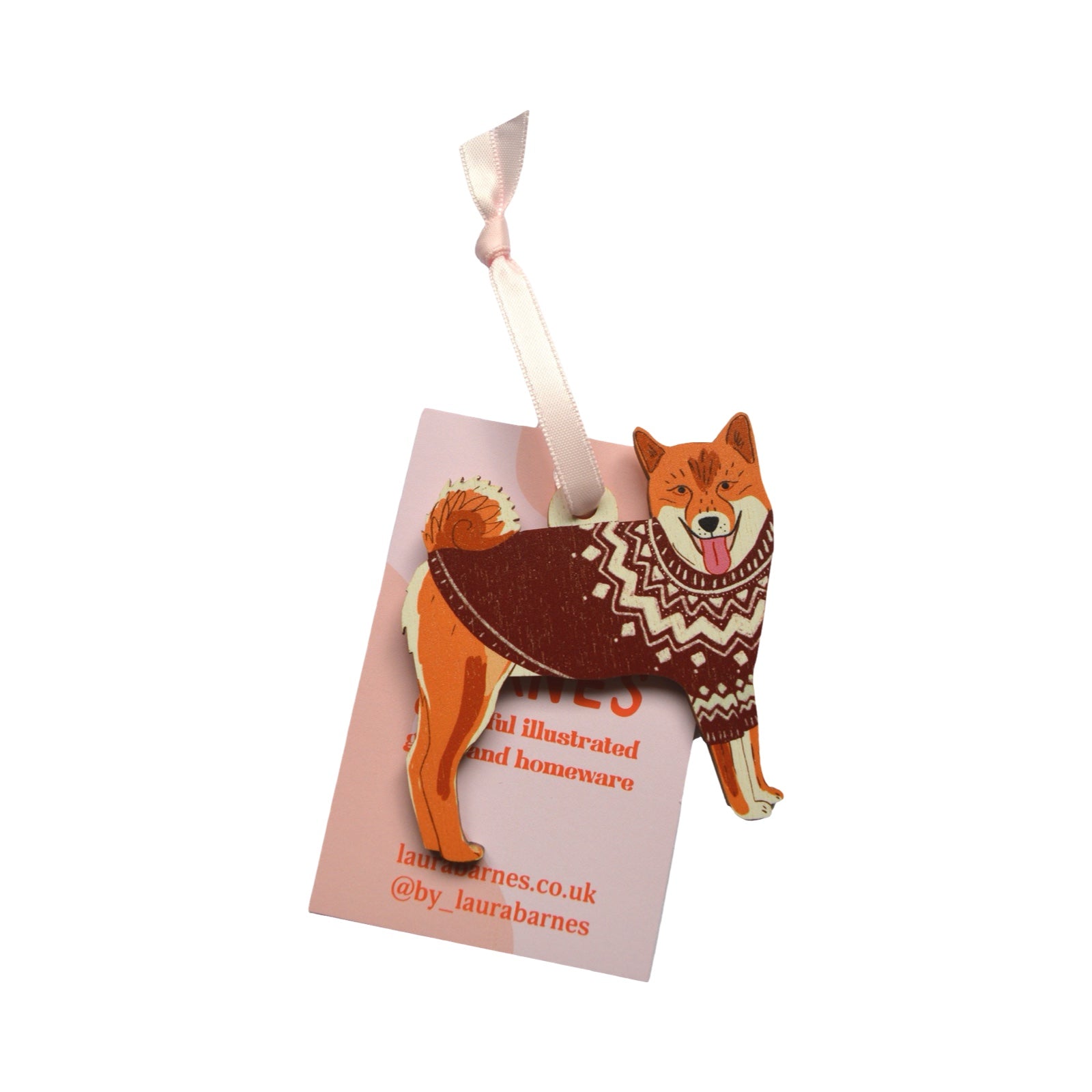 Dog-shaped ornament with a patterned sweater on a pink card with branding.