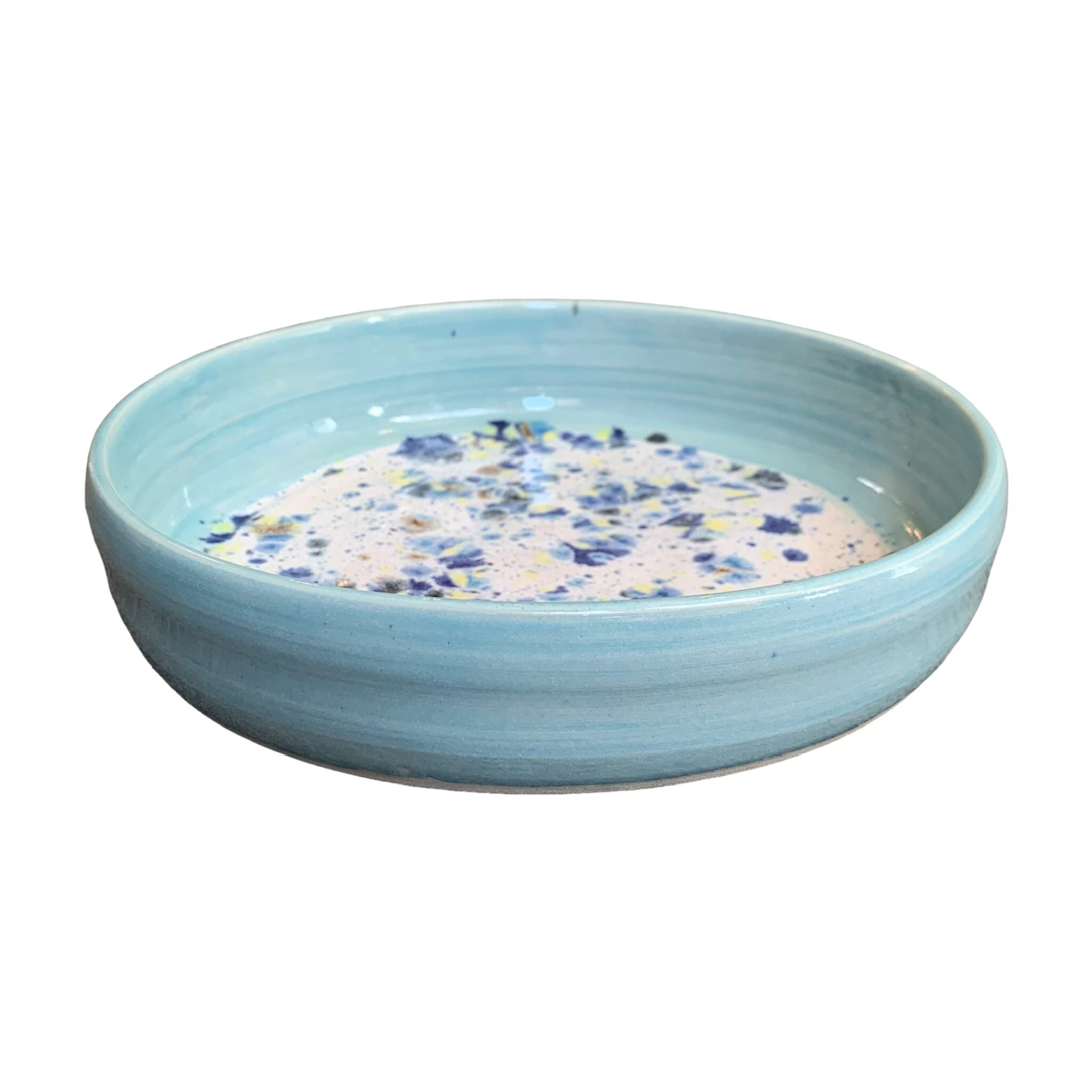 The side of a ceramic pasta bowl with a turquoise edge and a navy, yellow and white shoreline pattern in the centre.