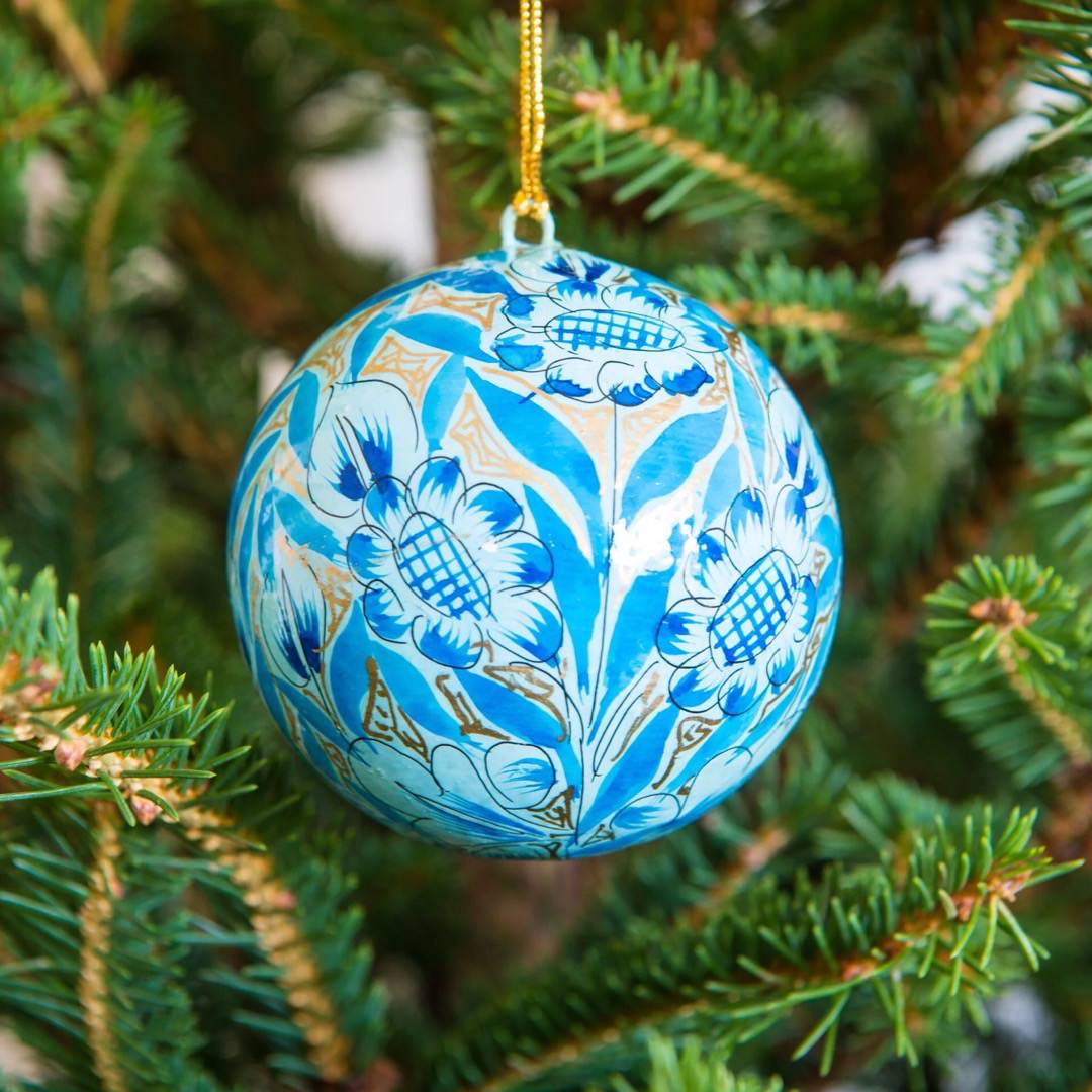 A round papier mache bauble in gold with a sky blue and turquoise floral design hanging on a Christmas tree.