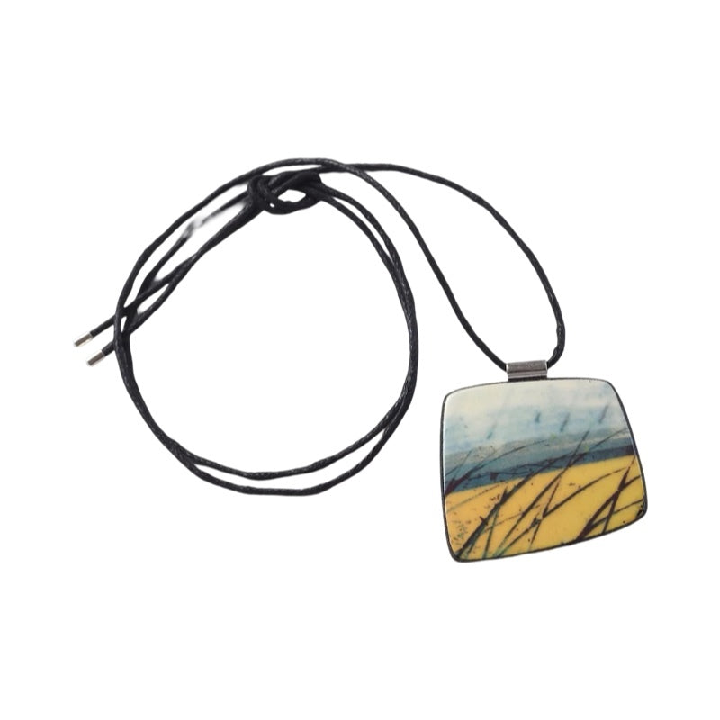 This pendent necklace is made from black porcelain casting slip layered with a white decorating slip and a ceramic decal, it is a wearable piece of art! The pendent has a yellow, blue and black abstract pattern, inspired by fields and coastlines