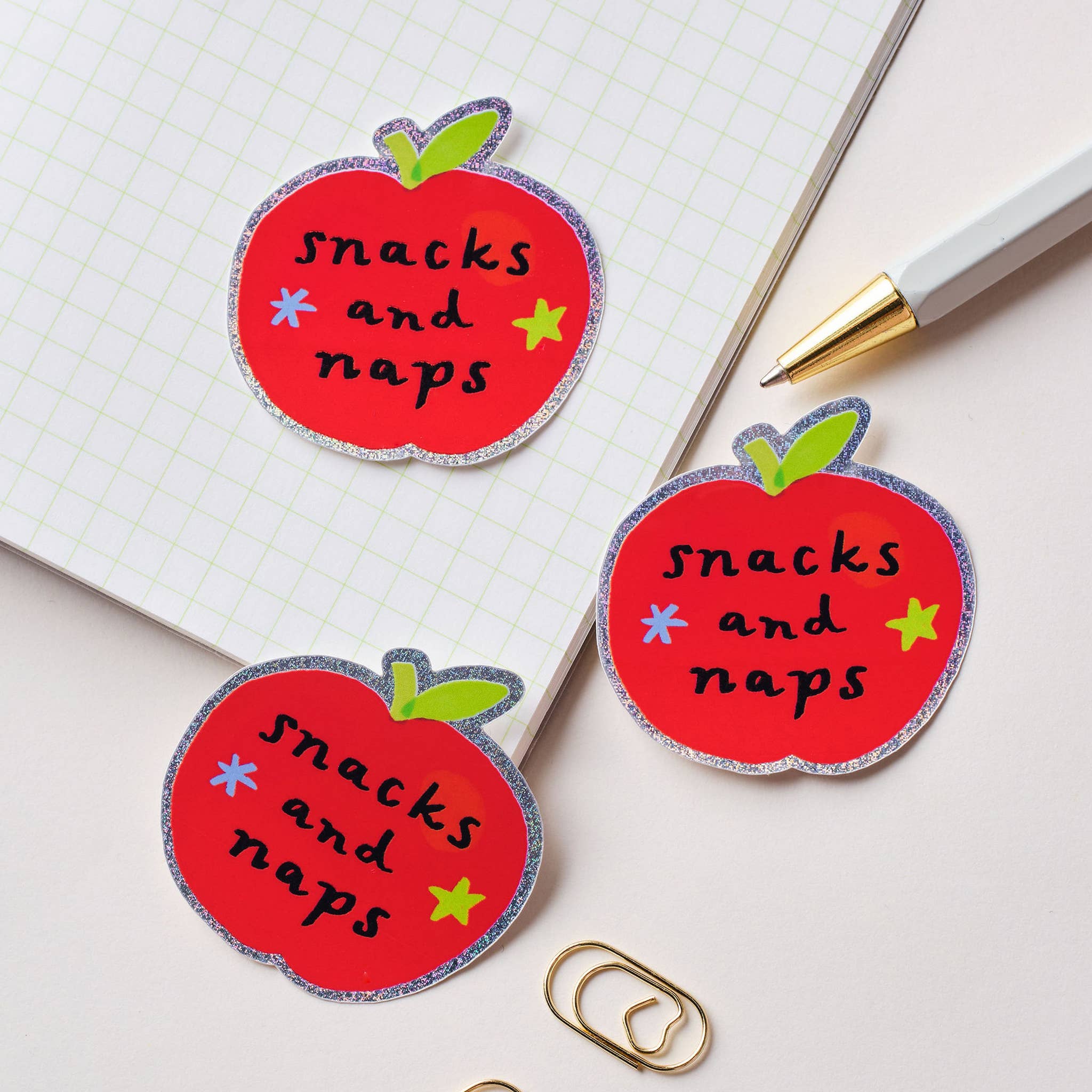 Three red apple-shaped stickers with 'snacks and naps' text on a notebook page.