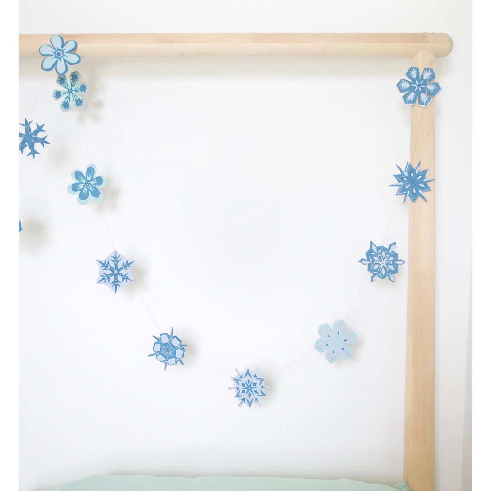 A snowflake paper garland with 20 screen-printed paper snowflakes in various blue and silver designs hanging from a wooden frame.