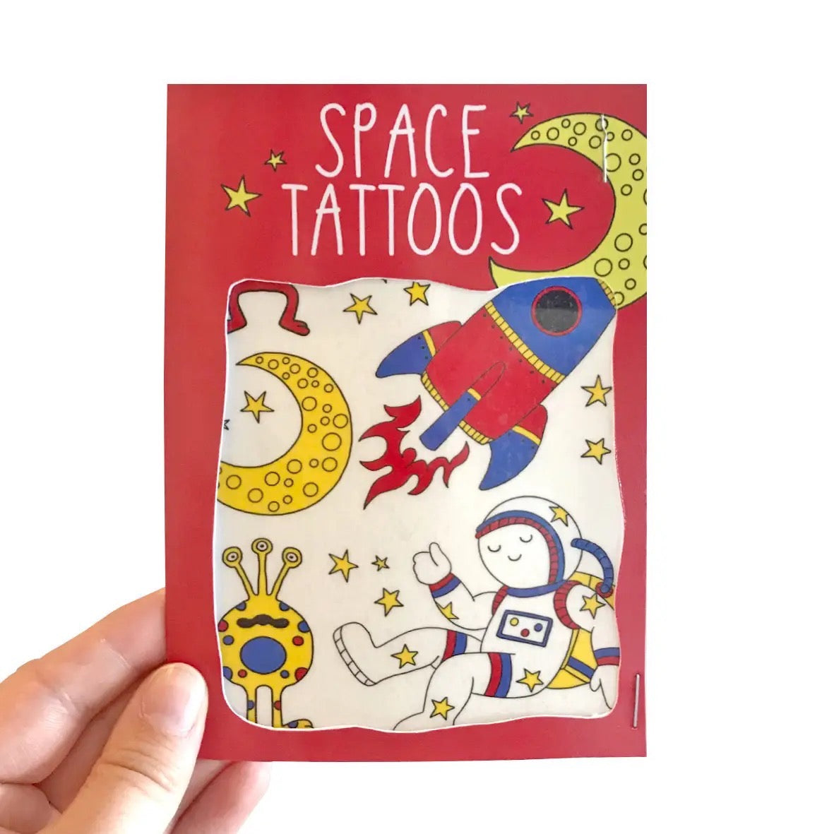Space-themed tattoo book with illustrations of an astronaut, rocket, and alien on a red background, held by a hand.