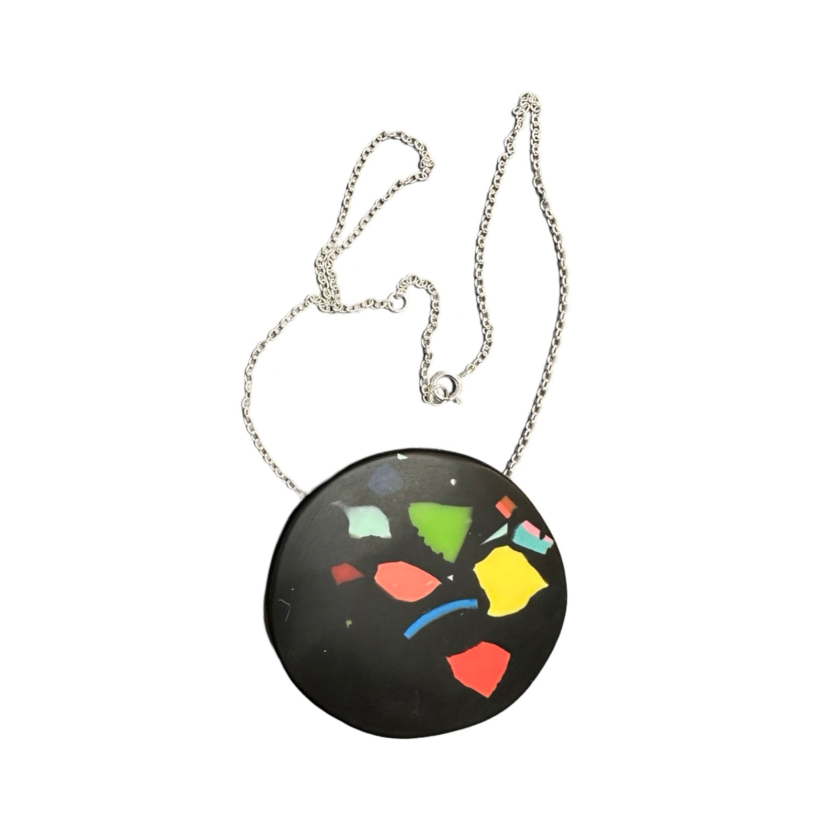 A black circular pendant with colourful resin speckles on a silver chain.