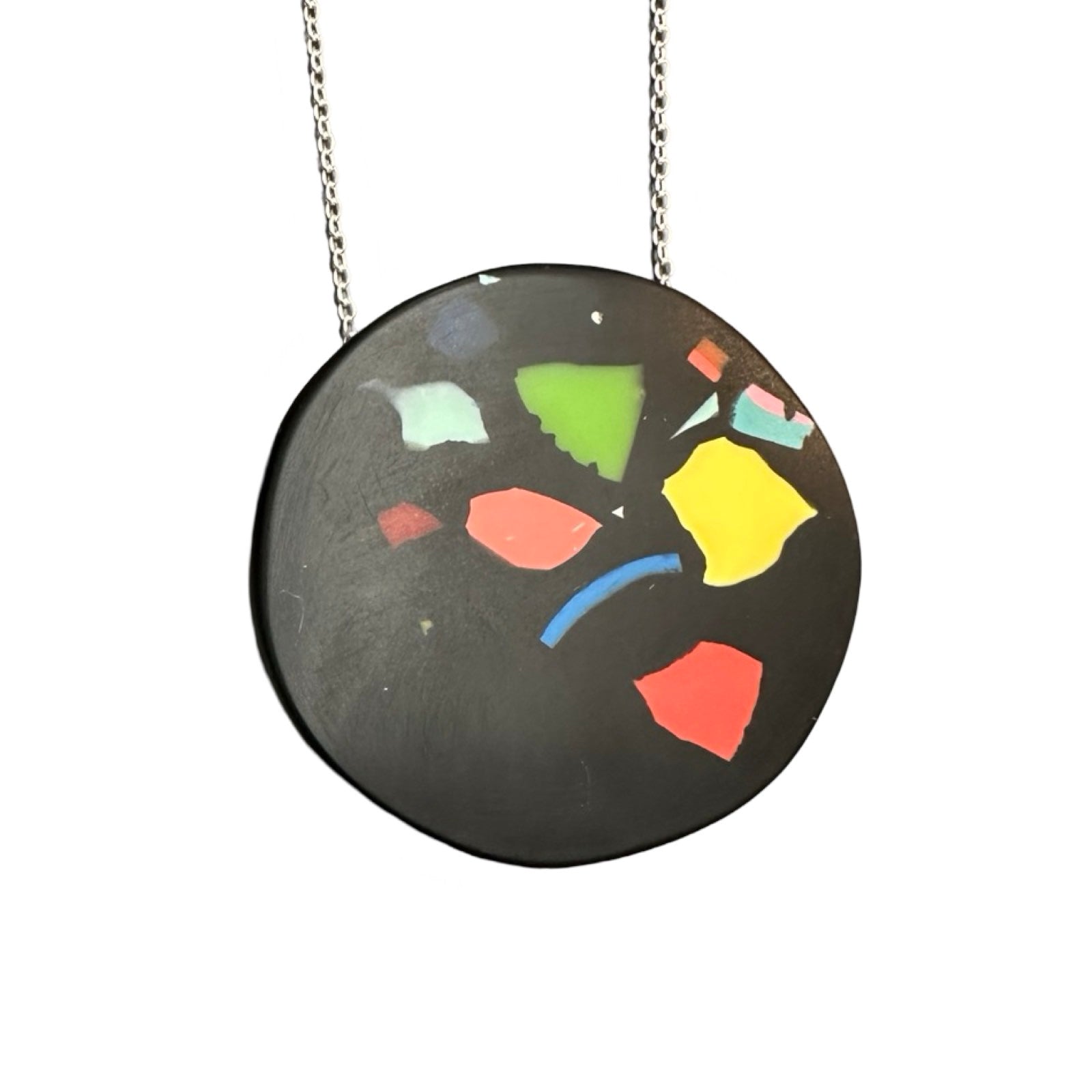 A black circular pendant with colourful resin speckles on a silver chain.