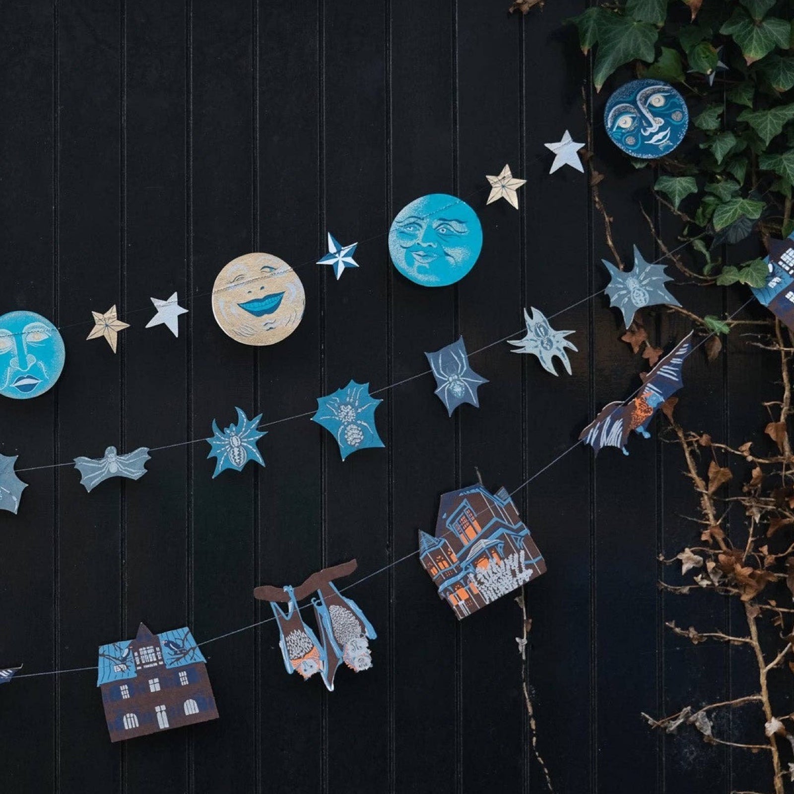 A spider paper garland with 20 screen printed spiders hanging in the middle of a man in the moon garland and a haunted house garland.