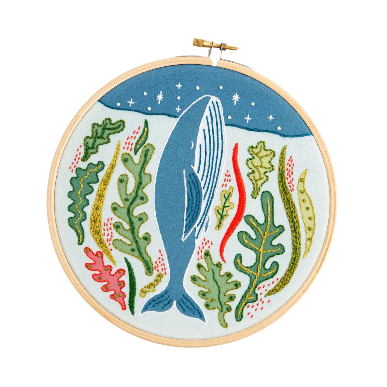 This craft kit teaches you to embroider a hoop with a whale surrounded by underwater plants pointing towards a sky full of stars.