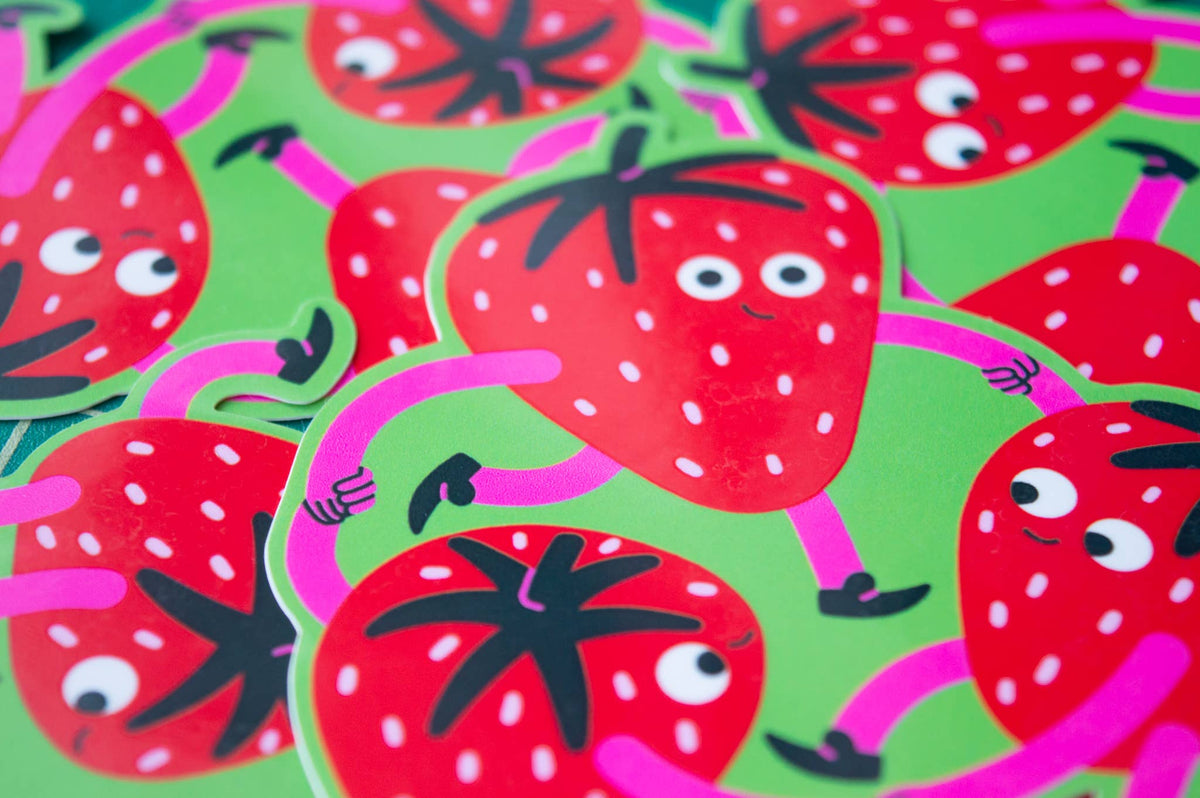 A close-up of die-cut stickers featuring cartoon red strawberries with white seeds, pink limbs, and black leafy tops on a bright green background.
