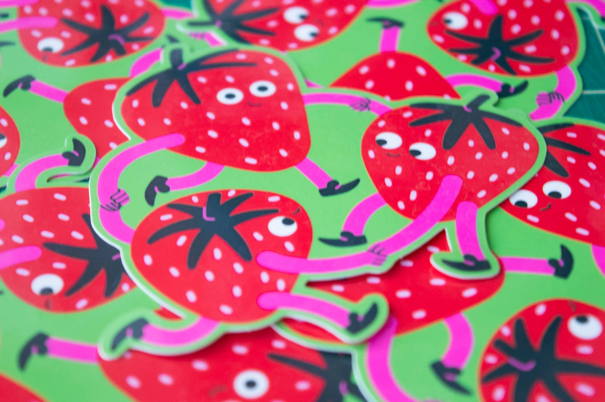 A close-up pile of die-cut stickers featuring cartoon strawberries with pink limbs and white eyes on a bright green background.