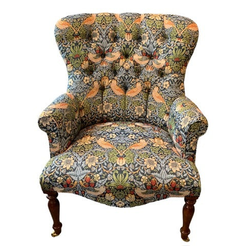 A hand-crafted occasional armchair covered in William Morris-inspired strawberry thief fabric, with a button-back and cream binding, mahogany legs, and gold castors.
