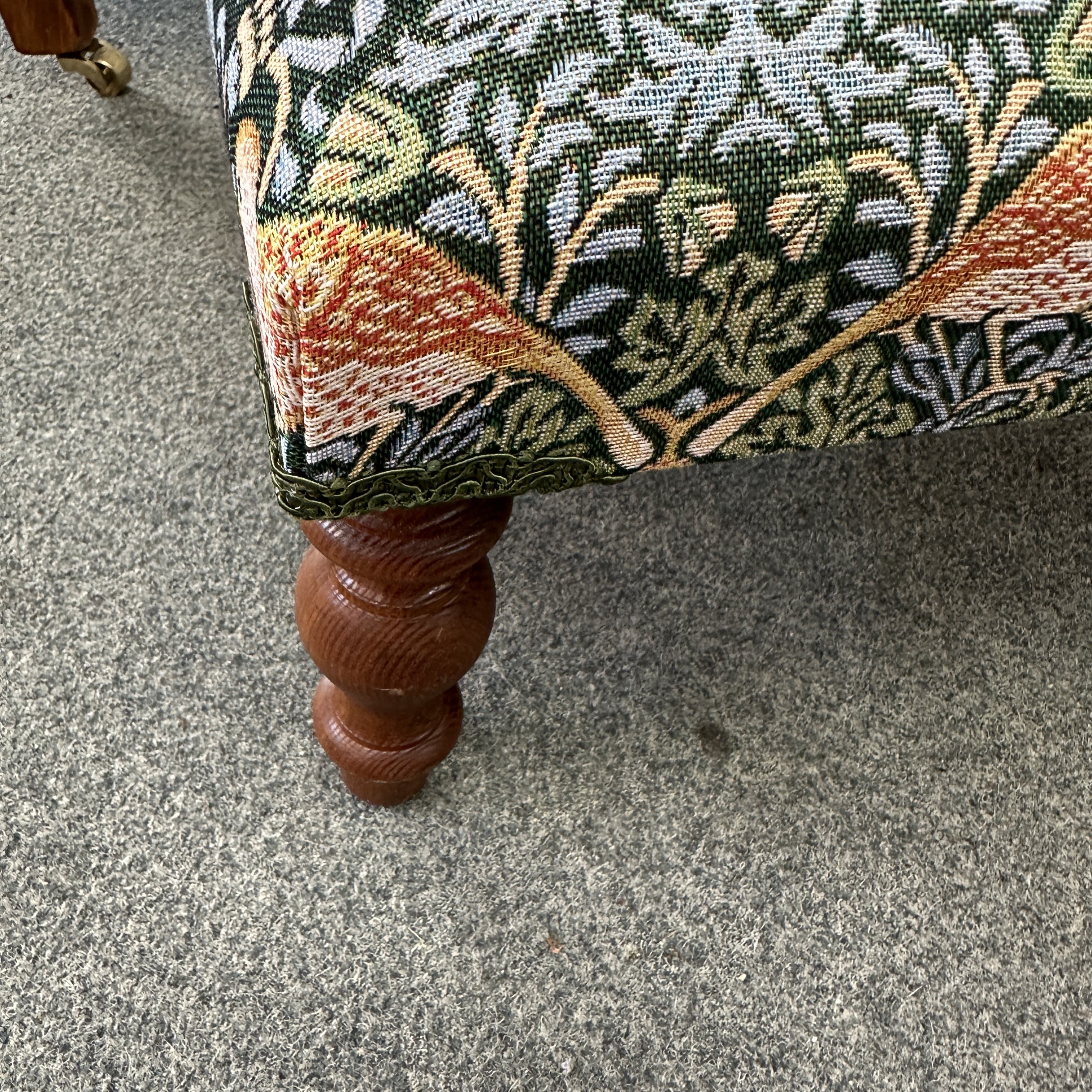 Close-up of a upholstered chair leg with decorative fabric on a carpeted floor.