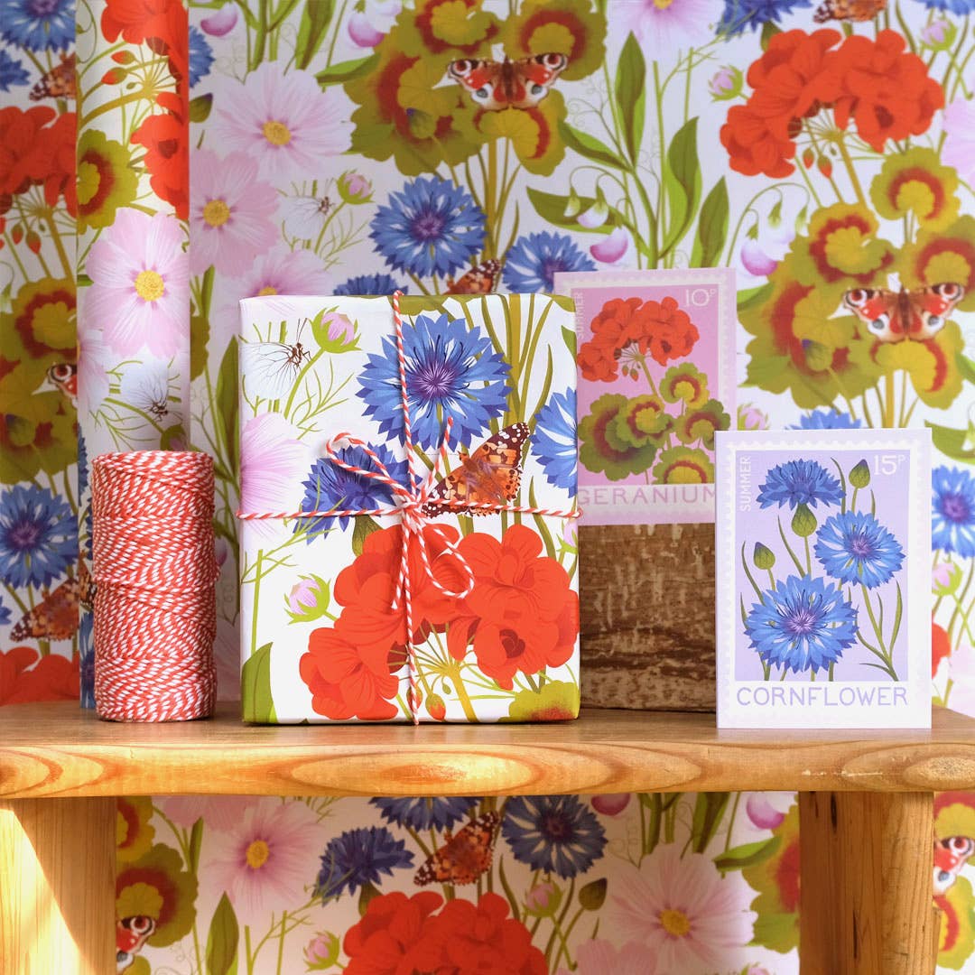 Floral-themed gift wrap and stationery items on a wooden surface with a colorful floral-patterned background.