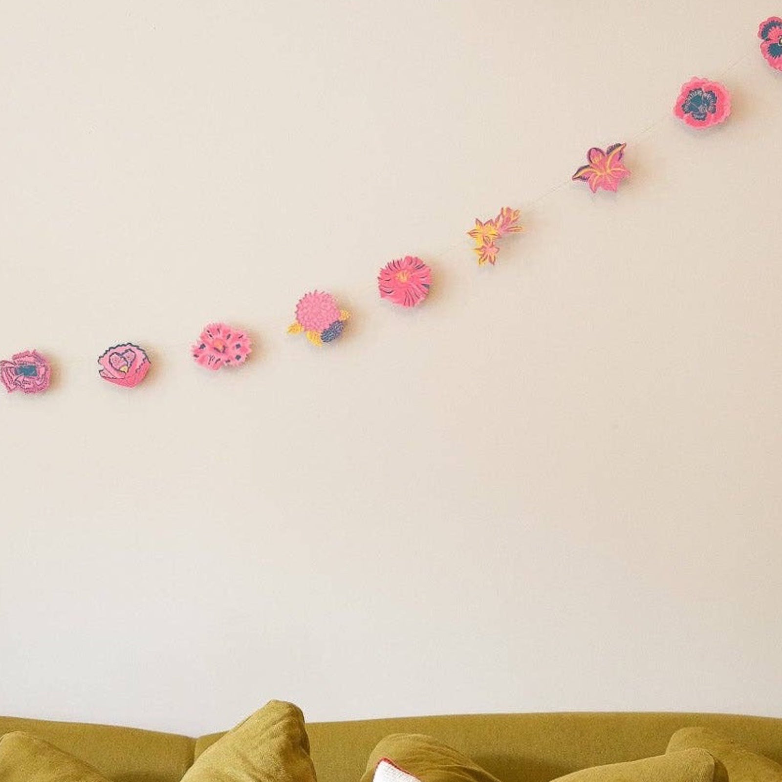 A summer garden paper garland featuring twenty screen-printed floral designs in shades of pink, teal and mustard hanging along a cream wall.