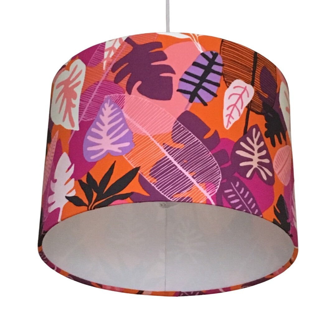 Drum lampshade with an orange background and a variety of pink, white, black and purple leaves.