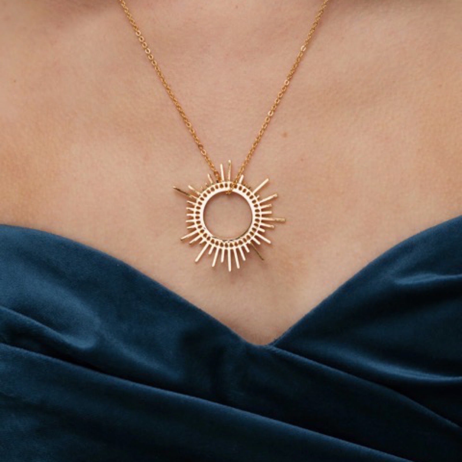 An image of a golden sun shaped necklace against a white background.