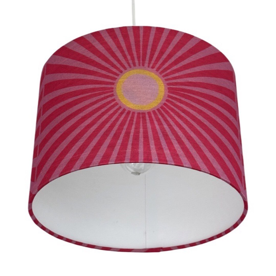 Close up of a drum lampshade covered in pink cotton/linen blend fabric with pale pink and yellow suns and pale pink sunbeams