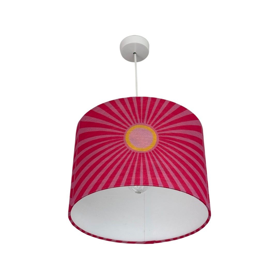 Drum lampshade covered in pink cotton/linen blend fabric with pale pink and yellow suns and pale pink sunbeams