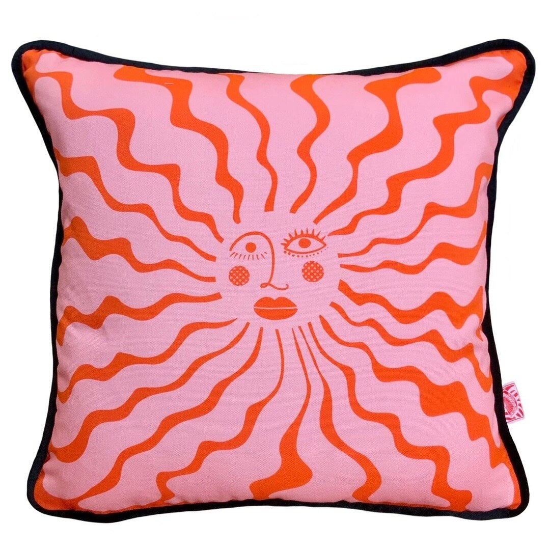 Cushion with an illustration of the sun in pink and red with a face in the centre.