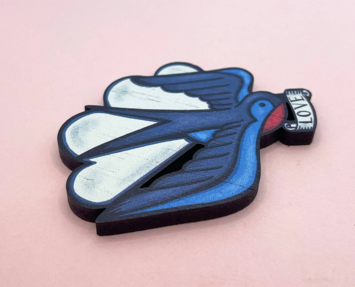 Blue bird-shaped brooh with 'LOVE' on a pink background