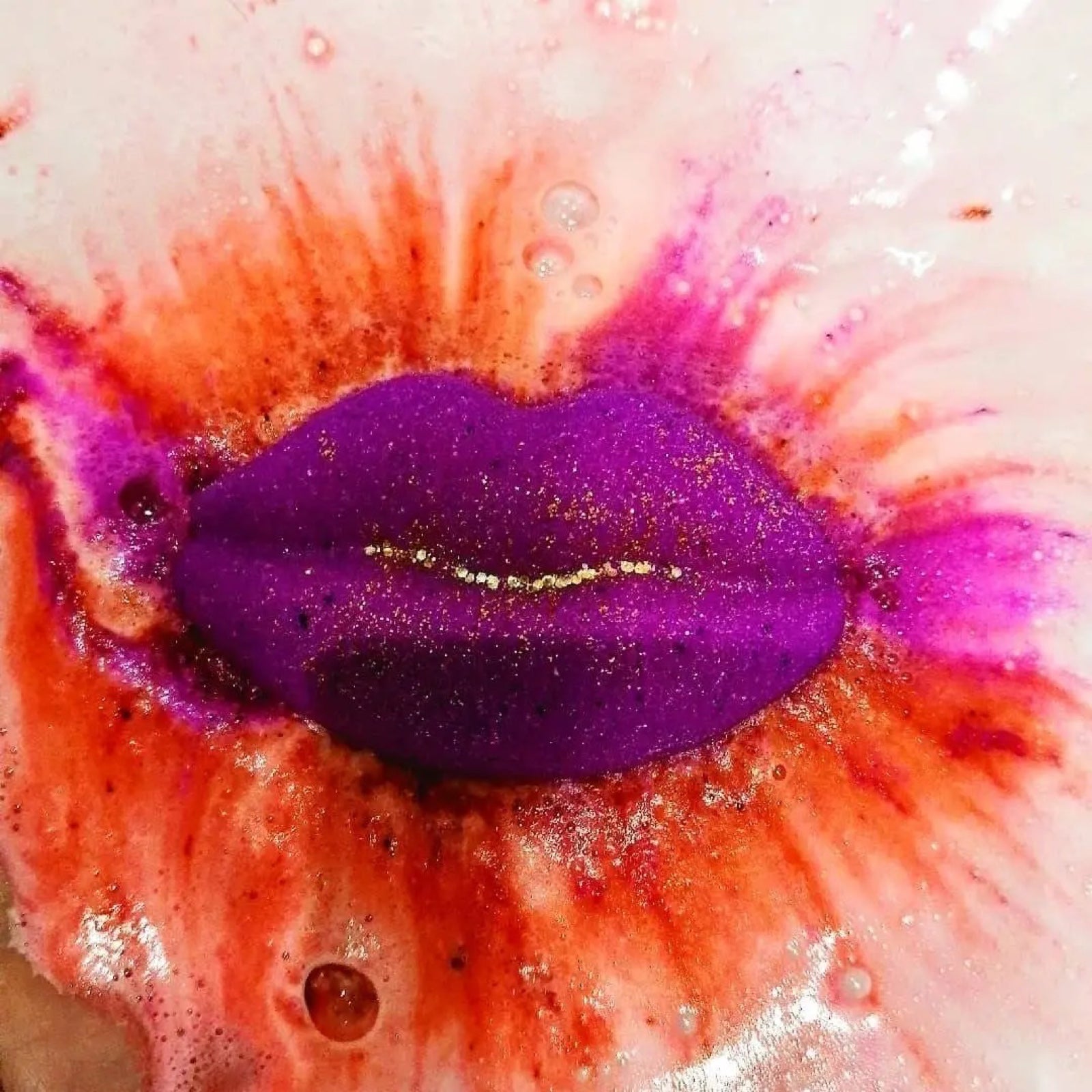 A pink lip shaped bath bomb dissolving in thebath water and turning it red, pink and white